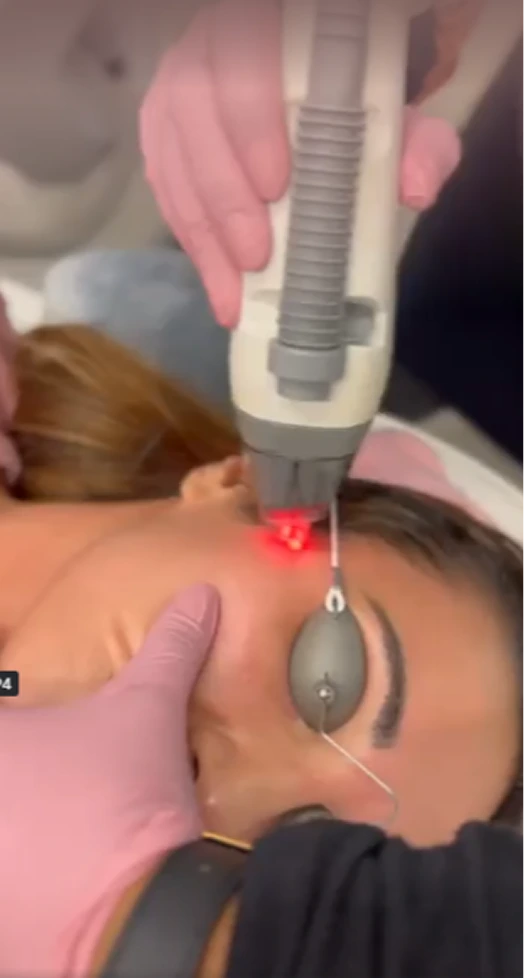 Practitioner in pink gloves applying laser device emitting red light to patient's back during treatment