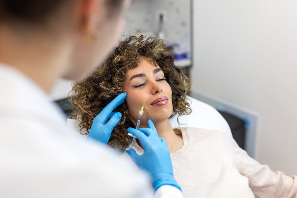 Provider in blue gloves administering injectable treatment to patient's cheek in clinical setting