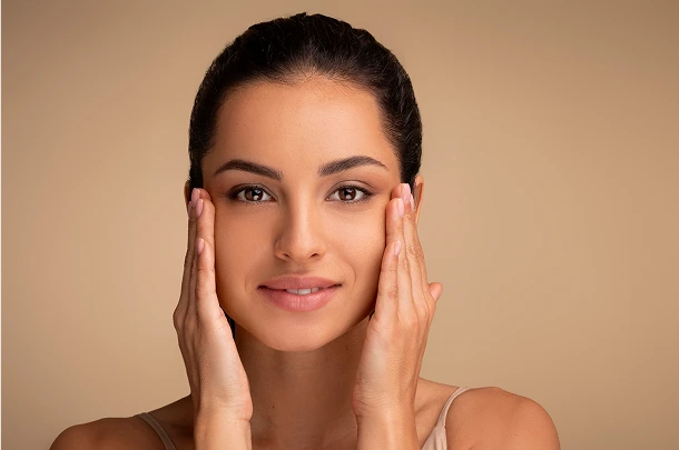 Woman with hands framing her face, looking directly at camera with a smile