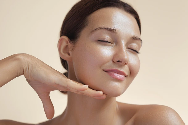 Woman with glowing skin touching her cheek, eyes closed with a satisfied expression