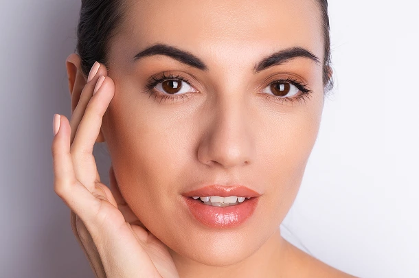 Woman touching her face, smiling toward camera with well-defined eyebrows and clear skin