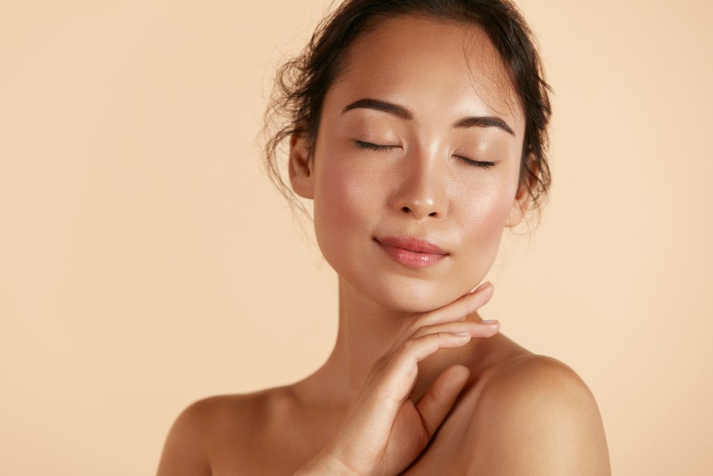 Woman with eyes closed touching her neck and jawline against a beige background